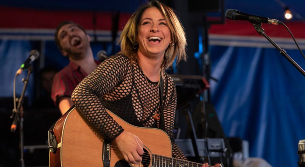 Lucy Spraggan laughing during a performance while playing guitar.