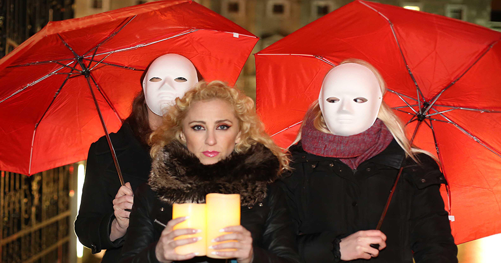 People in attendance at sex workers vigil wearing masks, holding red umbrellas and lit candles