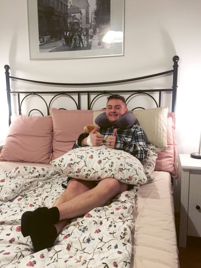 young trans man in bed showing thumps up after his top surgery