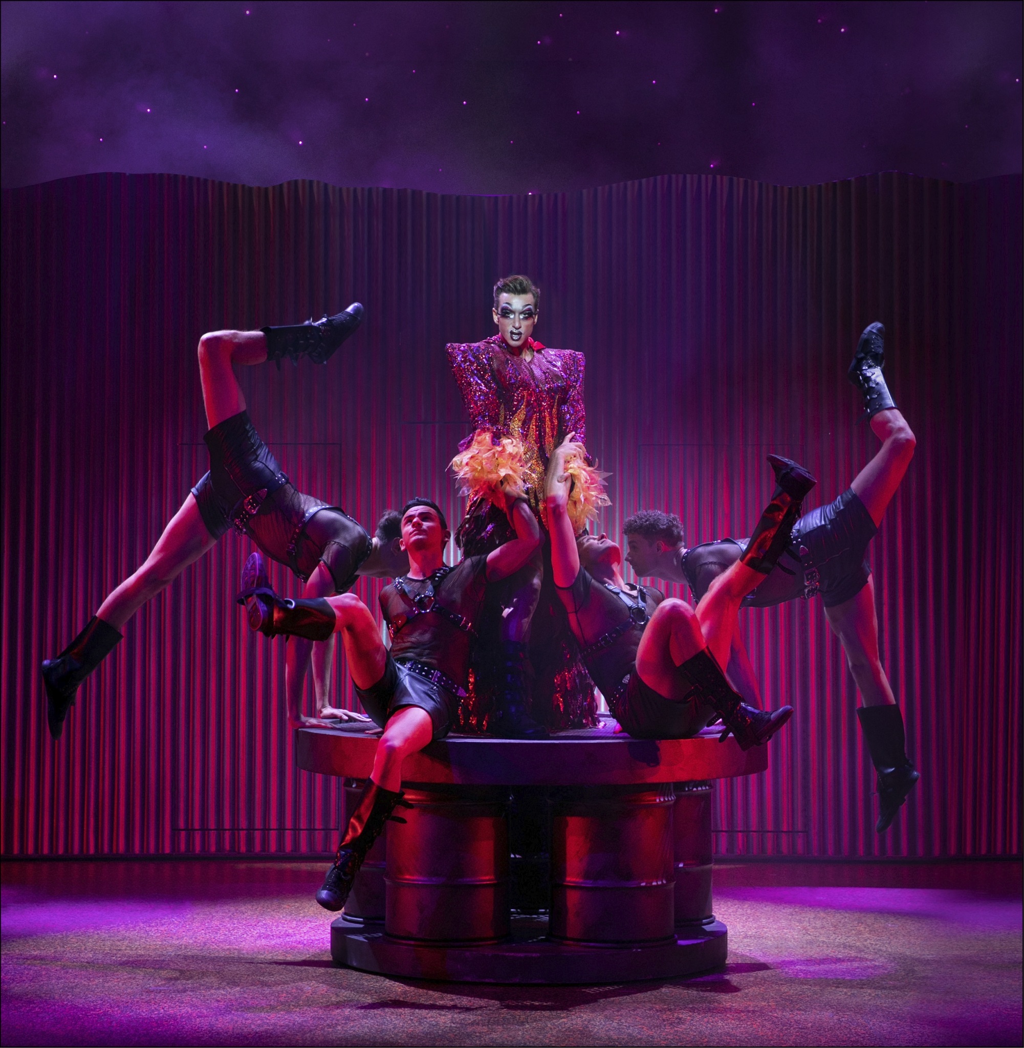 Main actor surrounded by men wearing black and harnesses in Priscilla Queen of the Desert