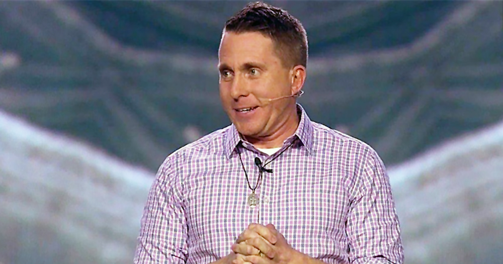 Chasity speak Jason Evert speaking in a conference wearing a red and white shirt and has his hands clasped