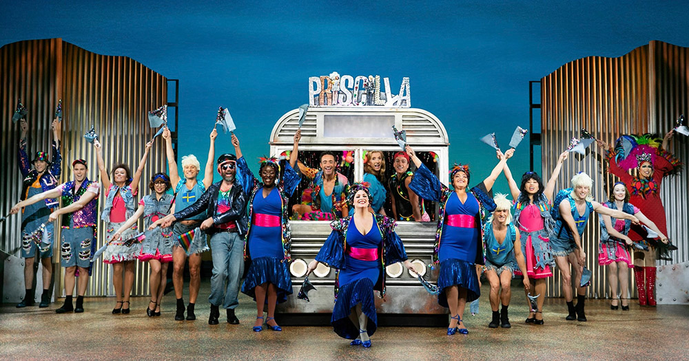 Cast of musical Priscilla Queen of the Desert standing in front of the iconic bus