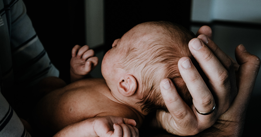A close up of a man's hands as he cradles a newborn baby