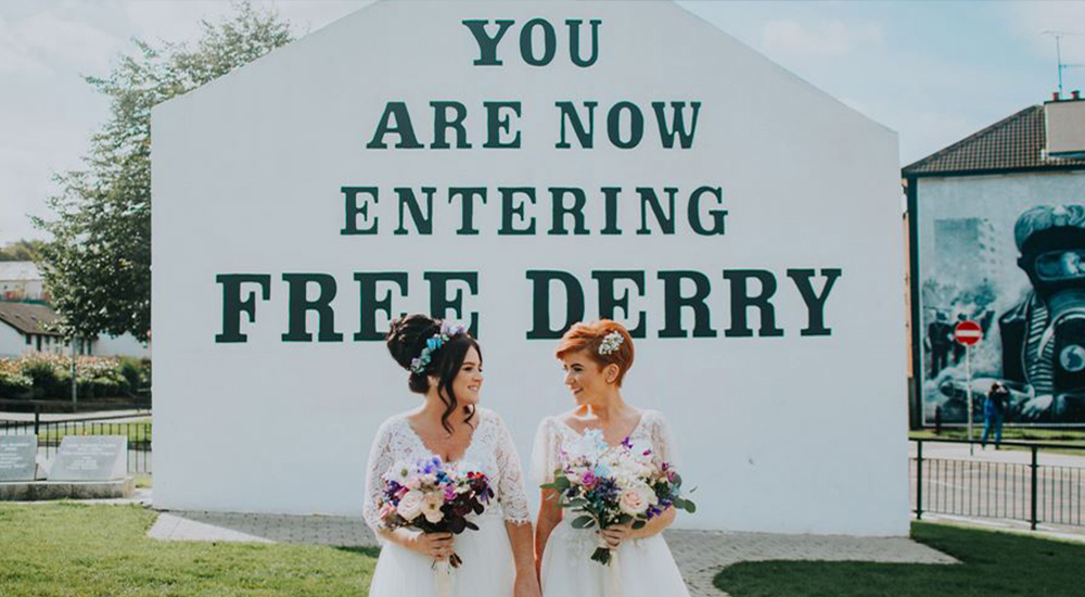Wedding photo of Emma Bradley and Danielle Doherty in front of the Free Derry Corner