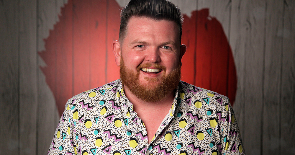 Podcast star James O'Hagan smiling in front of a wall with a painted heart as part of First Dates promo images