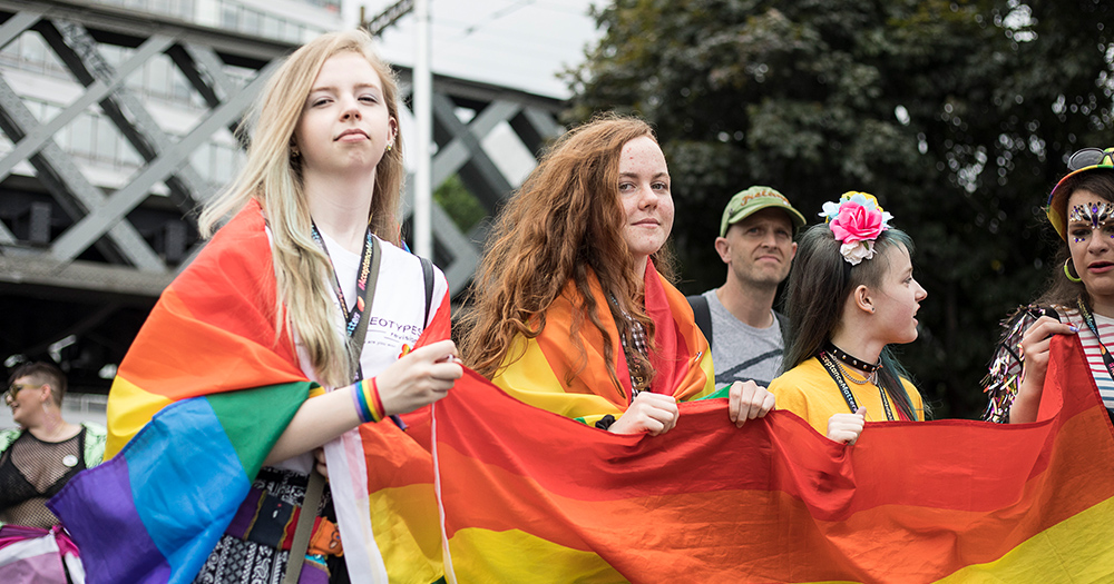 A group of young women holding a rainbow flag and marching in a Pride parade