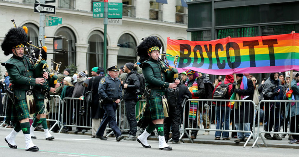 Two men playing bagpipes in St Patrick's Day Parade in Staten Island, while passing a pride flag with the words 'Boycott' on them