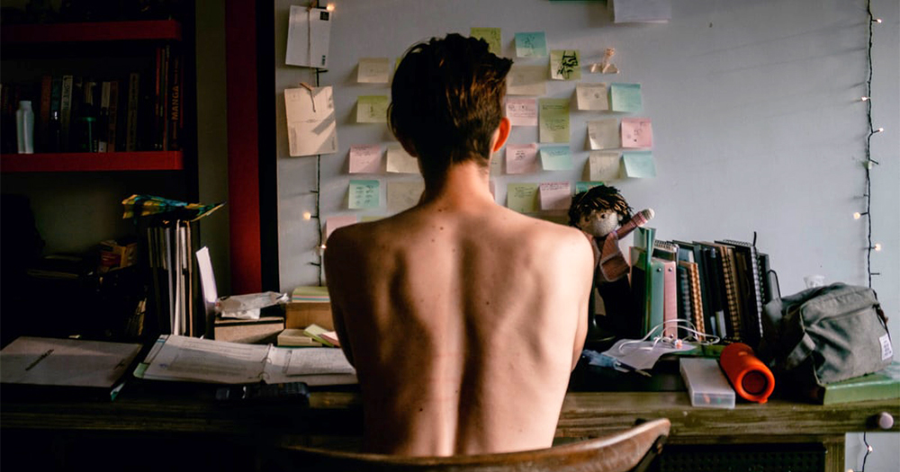 Back of a shirtless man sitting at a desk facing the wall. People are facing stress and anxiety during the COVID-19 outbreak