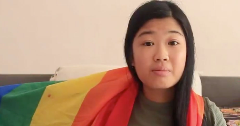 A young Indonesian woman in a room wraps herself in an LGBT+ flag