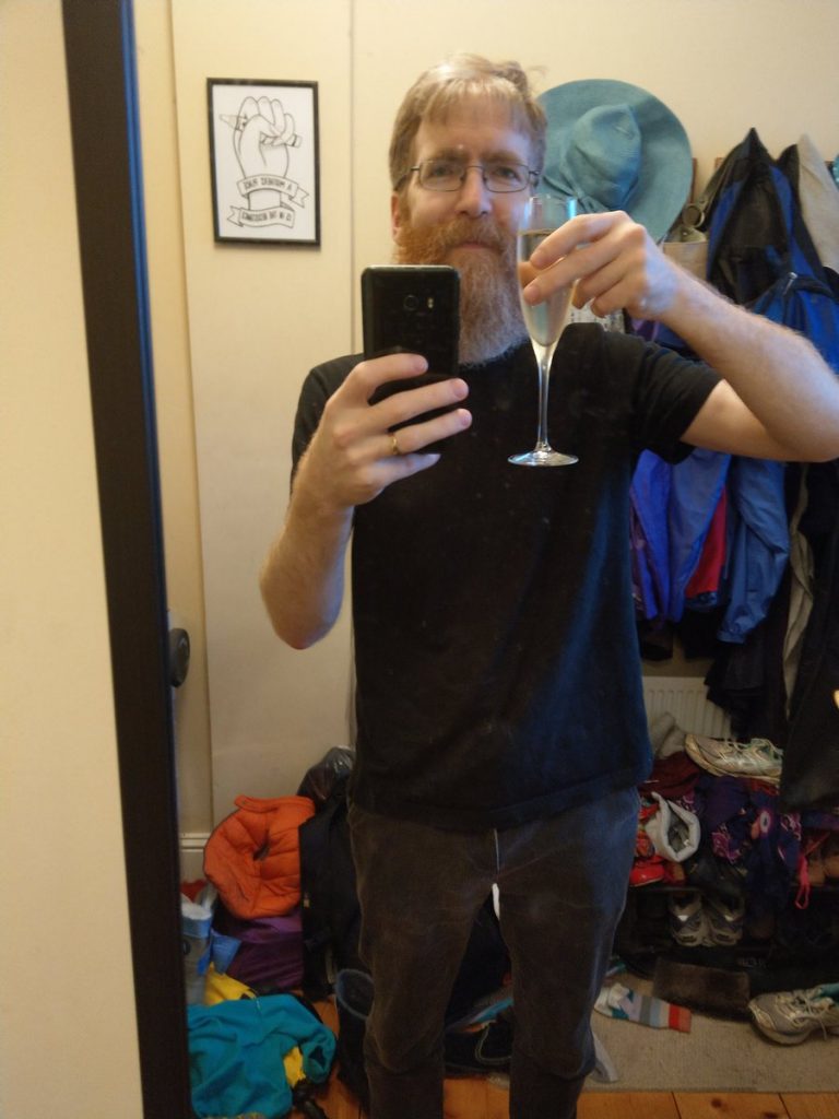 Jon Hanna taking a selfie in the mirror while holding a glass of shampain