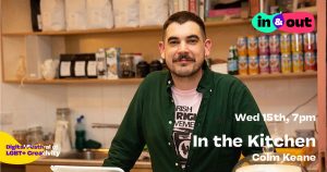 A smiling man with a moustache stands in front of a well stocked kitchen
