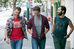 Three men walk down a city street, chatting and smiling