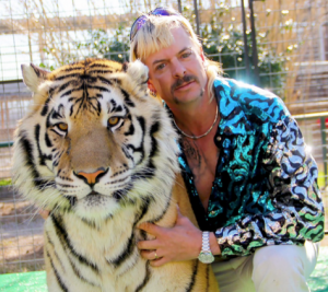 A man with a mullet dressed in 1980s style clothes leans against a huge tiger