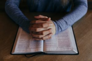 A close up image of a young man's torso as he sits with an open bible on a table