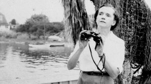 A woman standing by a pond with binoculars