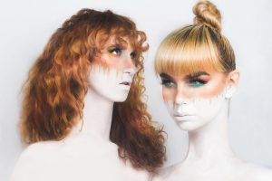 Two women with skin whited out by makeup, the colour orange painted around their eyes