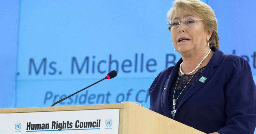 UN High Commissioner for Human Rights, Michelle Bachelet speaking at a podium, issuing a warning to not attack the LGBT+ community under COVID-19 emergency powers
