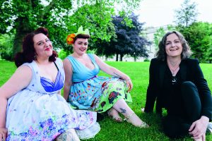 Three women sit on the grass in a park