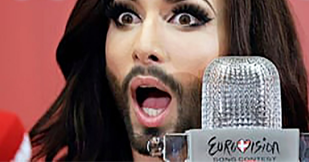 A drag queen with long hair and a beard gasps into a microphone