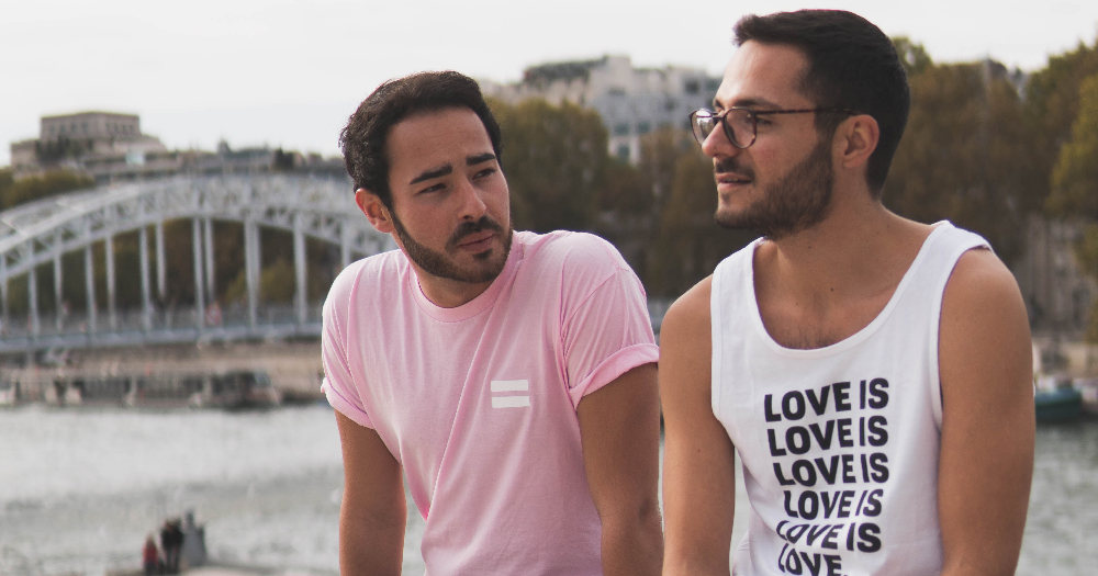 Two bearded young men look out across a river