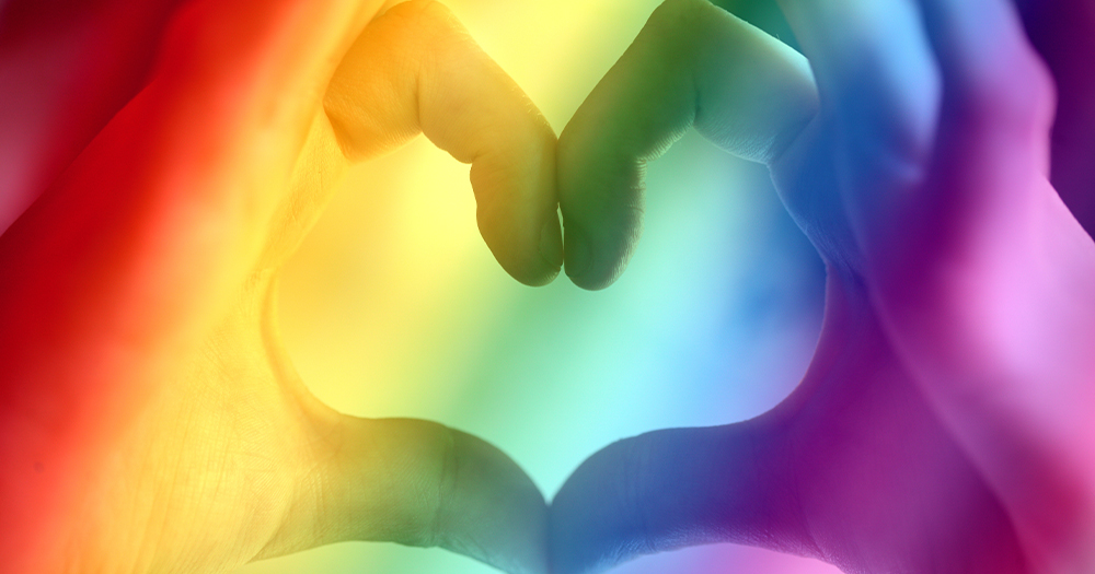 Hands forming the shape of a heart, everything is rainbow coloured