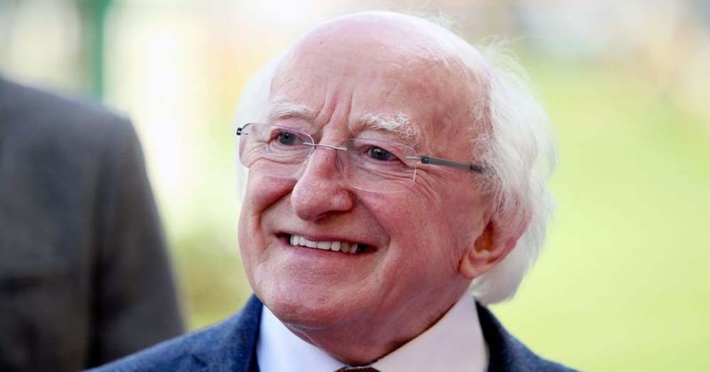 President Higgins, an older man with white hair and glasses, smiles for a photo