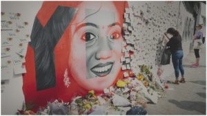 A woman leaves flowers at the painted mural of another woman on a wall