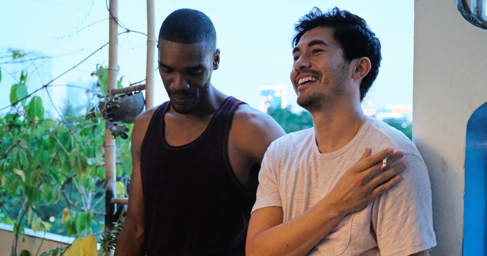 Actors Henry Golding and Parker Sawyers laughing during a scene from 2019 film Monsoon