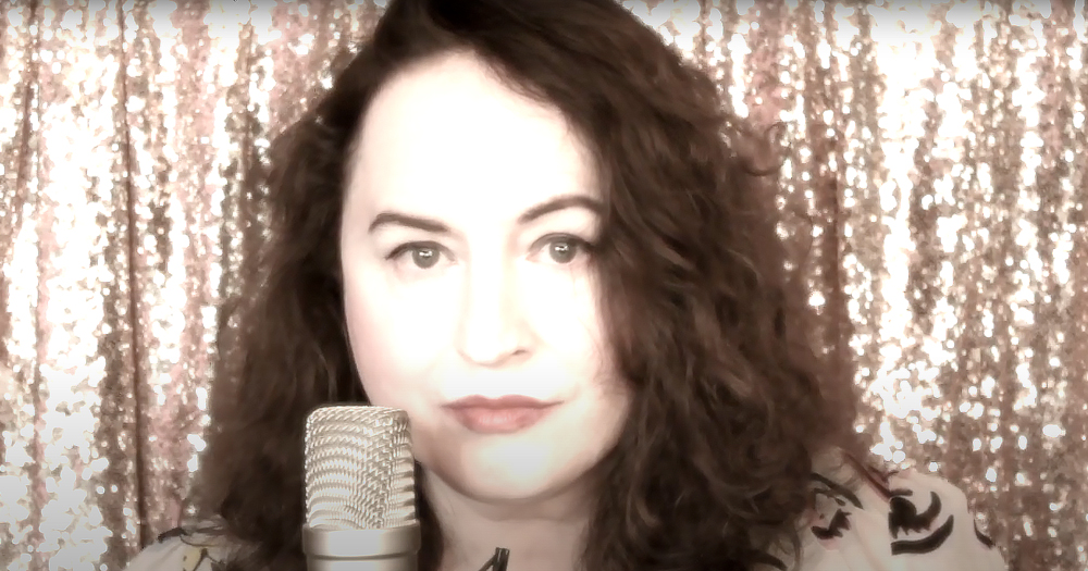 picture of a lady at a mic with shimmery curtains behind