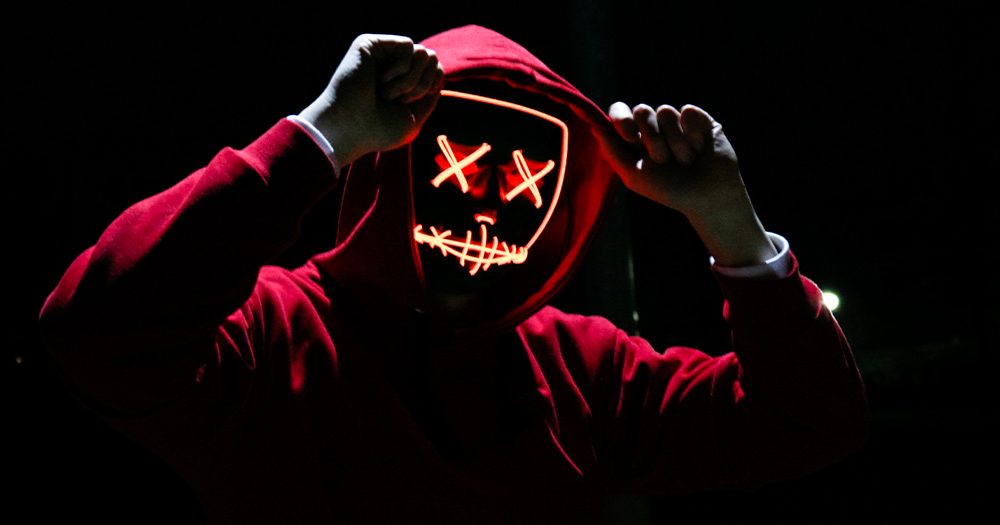 A hooded figure wearing a mask with lighted x's
