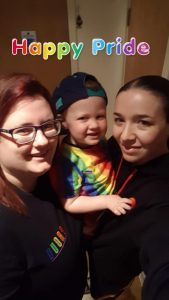 Two women hold their young son dressed in Pride colours