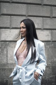 A woman in a suit and long hair walks down a city street