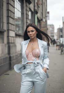 A woman with long hair wearing a suit walks down a city street