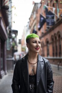 A young woman with green hair and tattoos looks into the distance