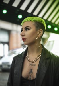 A young woman with green hair and tattoos looks into the distance