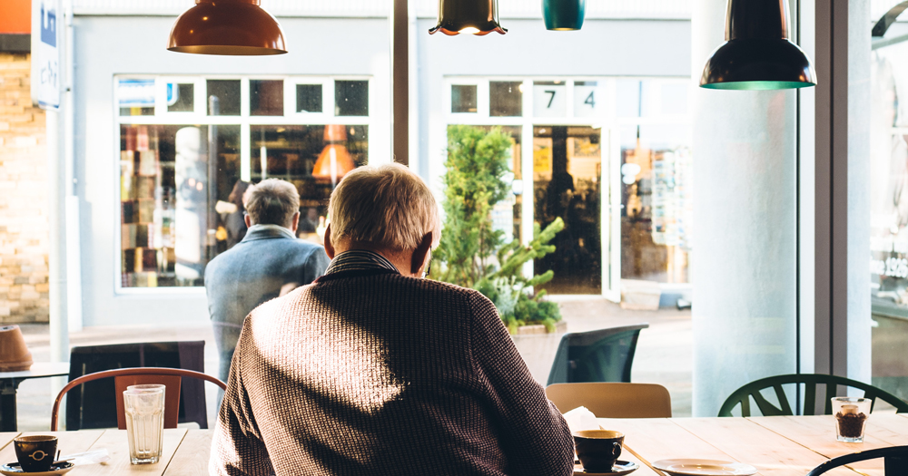 Two older men sit in a coffee shop, their backs to the camera