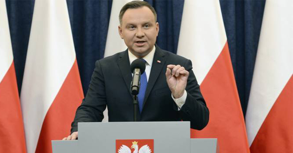 The Polish President Andrzej Duda, a middle aged man in a suit, speaks at a podium in front of Polish flags