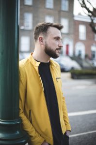 A bearded man leans against a lamp post