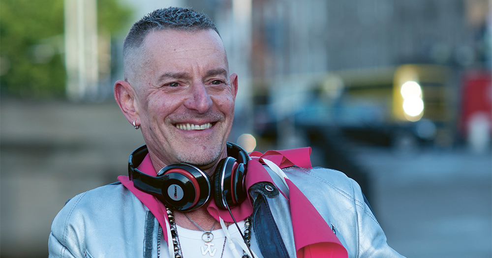 A smiling man with headphones around his neck in the middle of a city