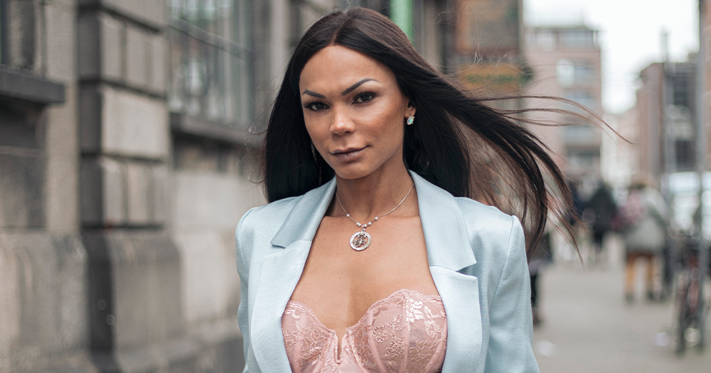 A woman with long hair wearing a suit walks down a city street