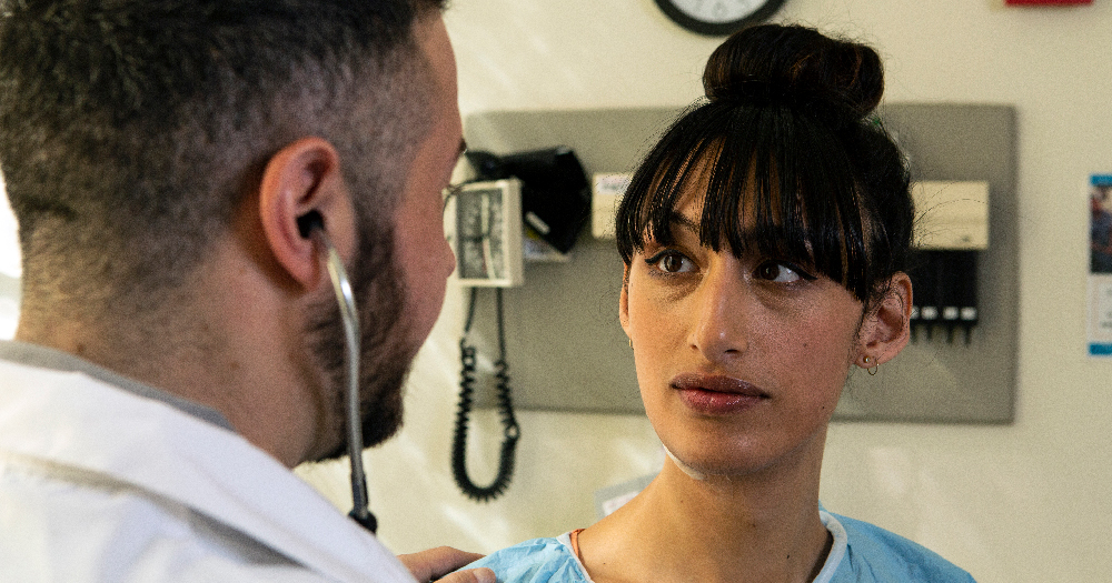 A transgender woman in a hospital gown having a conversation with a doctor, a transgender man