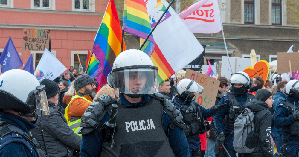 Police in Poland stand in front of a crowd waving rainbow flags
