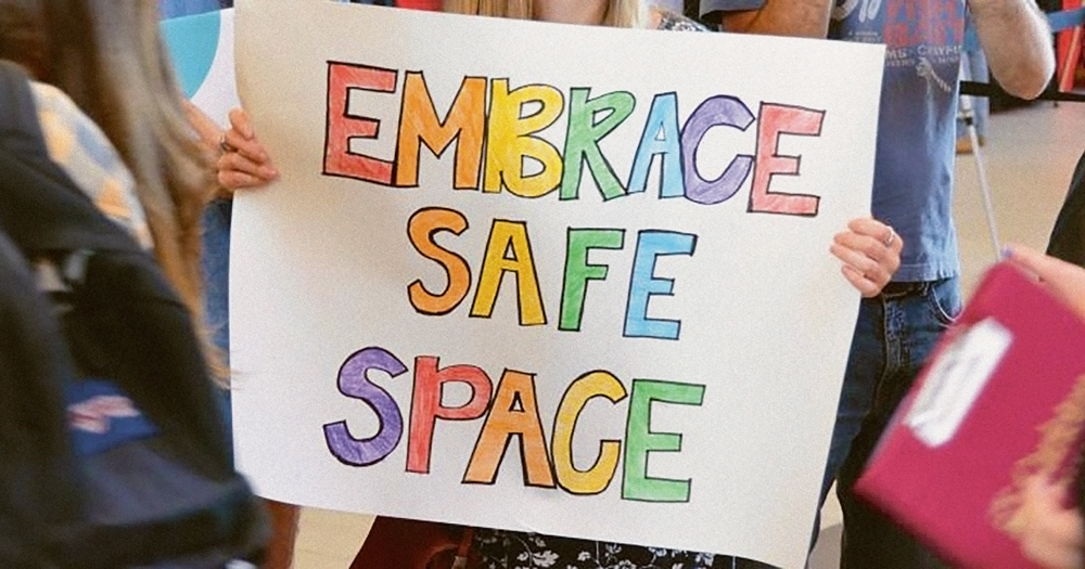 LGBT+ safe spaces - hands holding a sign that reads "Embrace safe space"