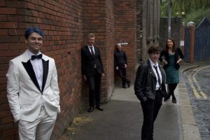 A group of people in formal dress stand around outside a building
