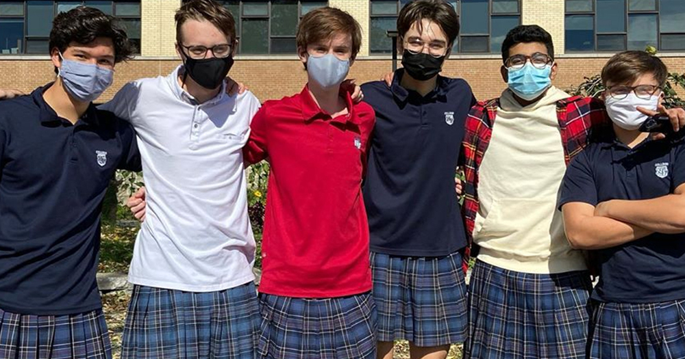 a group of male students wearing skirts pose for a photo