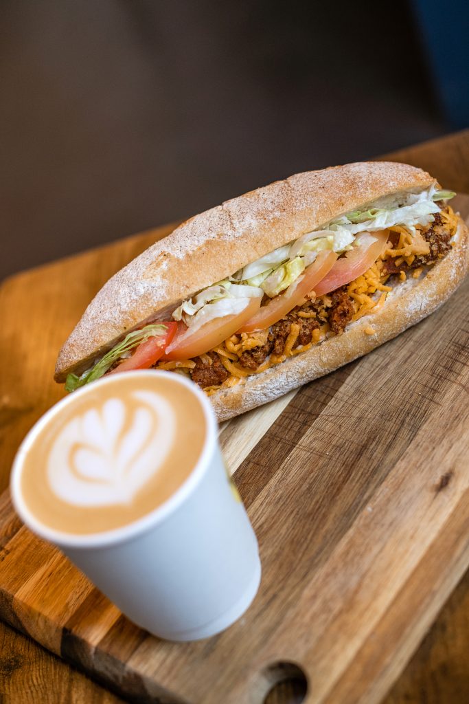 a coffee and chick*n fillet roll served on a wooden board at Vegan sandwich co