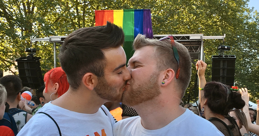 Two men kissing with a rainbow flag in the background