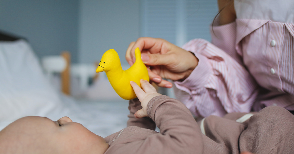 A mother holding a toy duck out to her baby