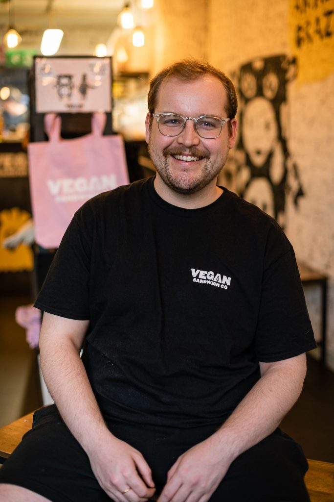 smiling man with glasses staring at the camera in the Vegan Sandwich Co