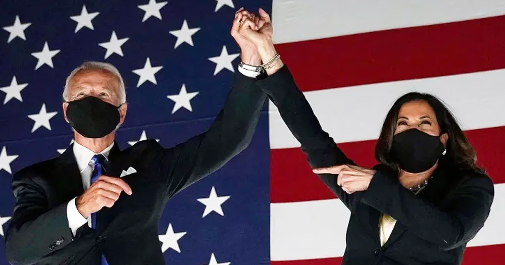 Joe Biden and Kamala Harris both wearing masks holding hands aloft in front of a US flag